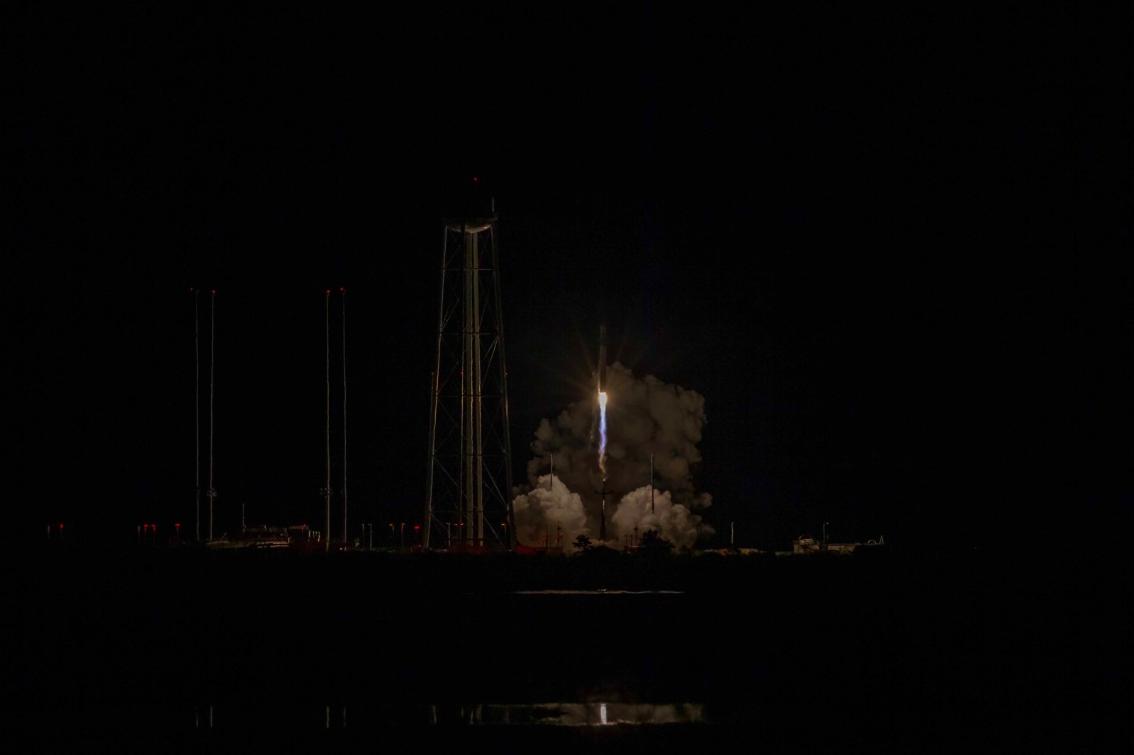 Electron lifts off at night from Wallops Island, with its exhaust lighting the pad and nearby water tower.