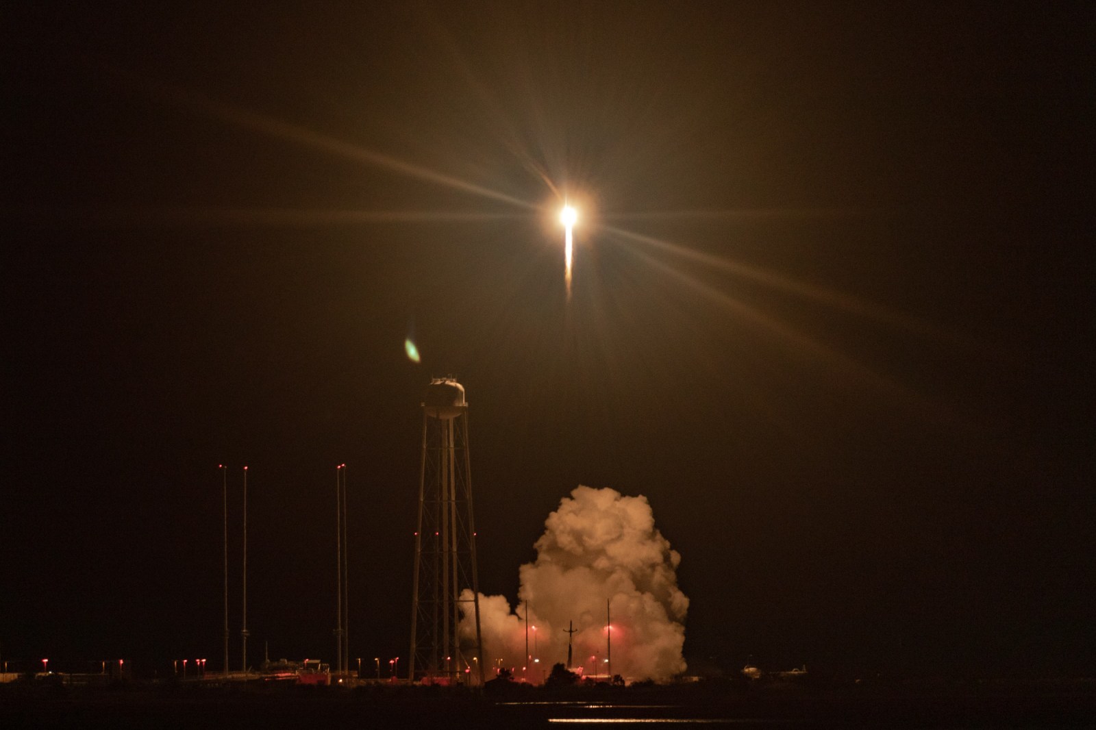 Electron lifts off at night from Wallops Island, with its exhaust lighting the pad and nearby water tower.