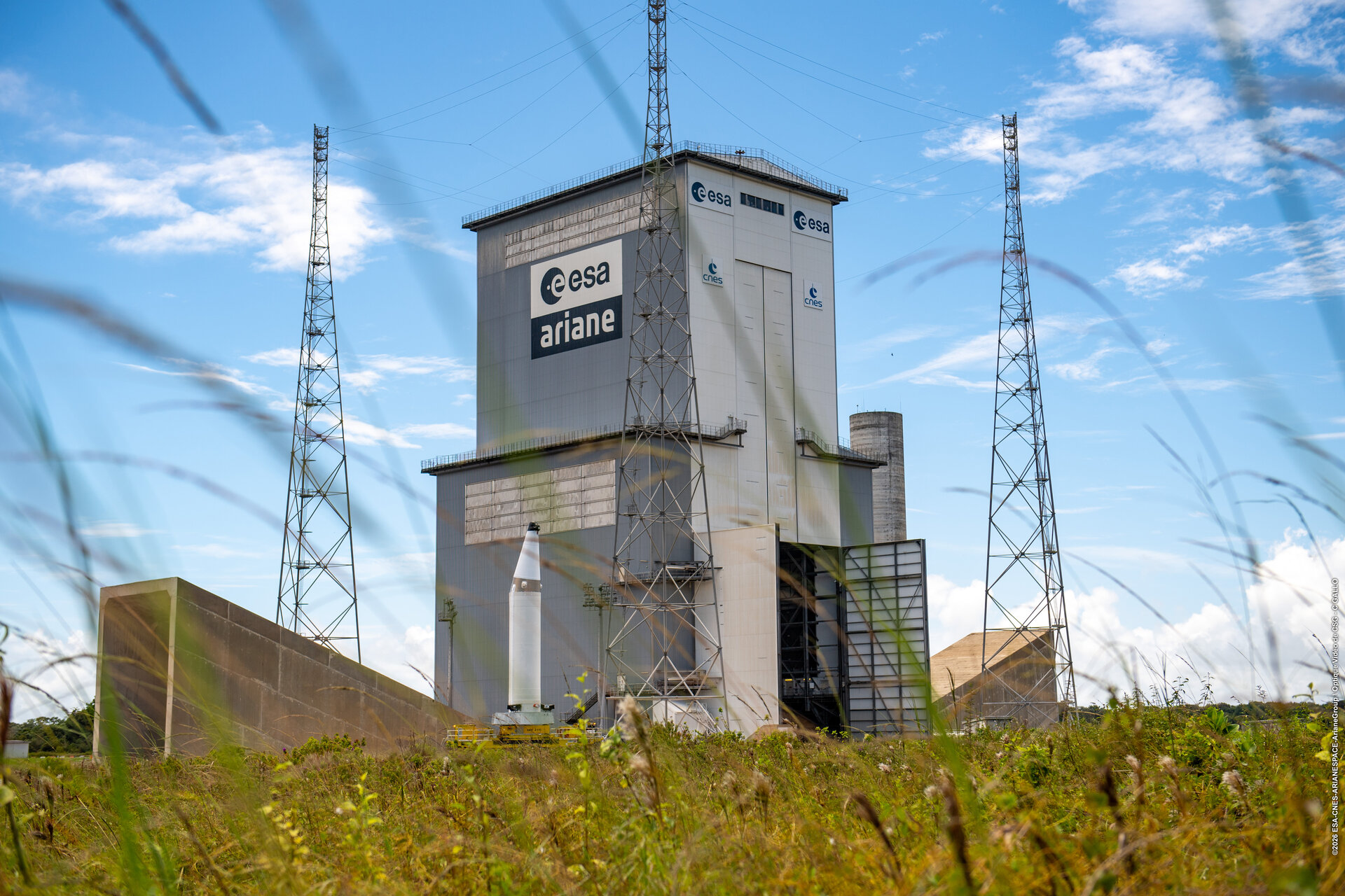 A white P160C booster stands beside Ariane 6’s tall mobile gantry at Europe’s Spaceport.