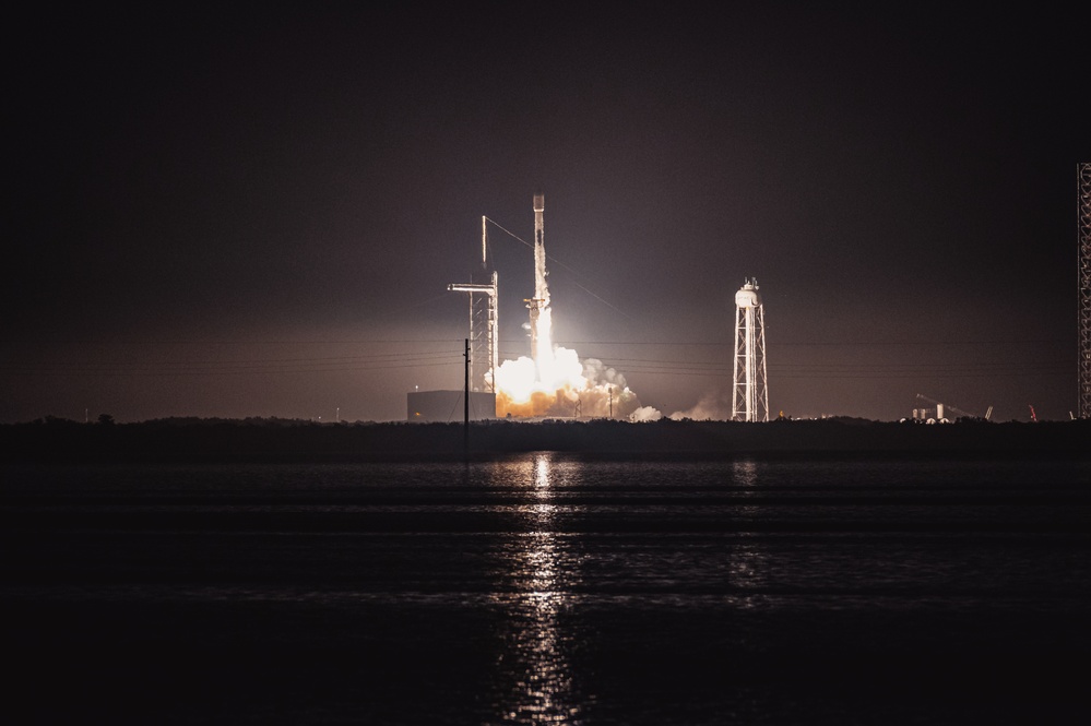 A Falcon 9 lifts off at night, its exhaust reflected in water at Kennedy Space Center.