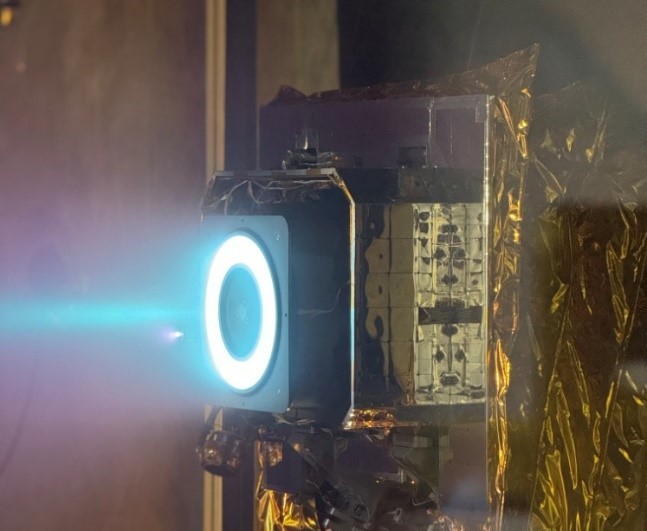 A bright blue plasma plume emerges from a circular thruster inside a ground-test installation.