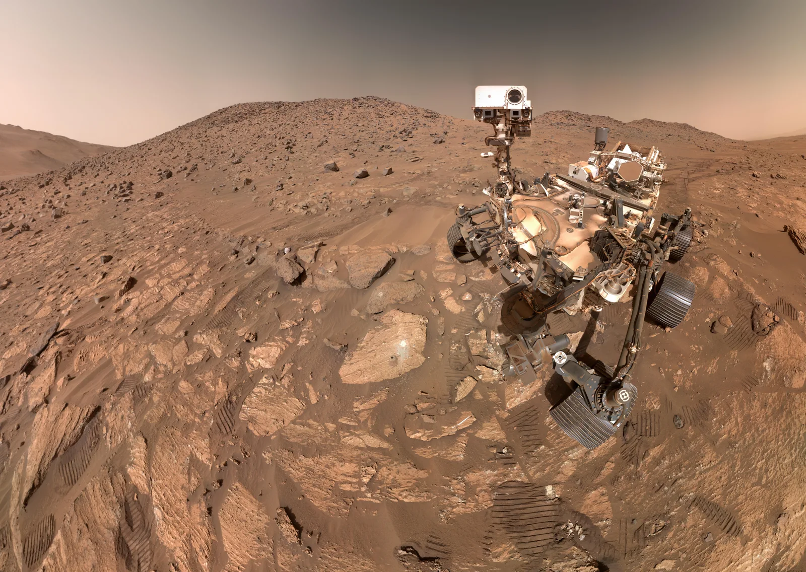 Perseverance rover on a rocky Martian plain beside Cheyava Falls, with hills behind it