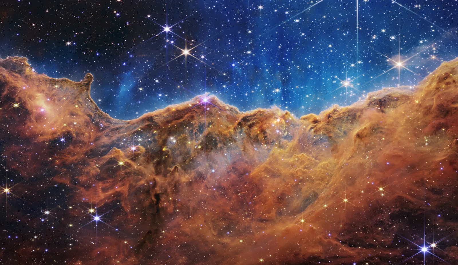 Golden ridges of gas and dust beneath a blue star-filled region in Webb’s Cosmic Cliffs image