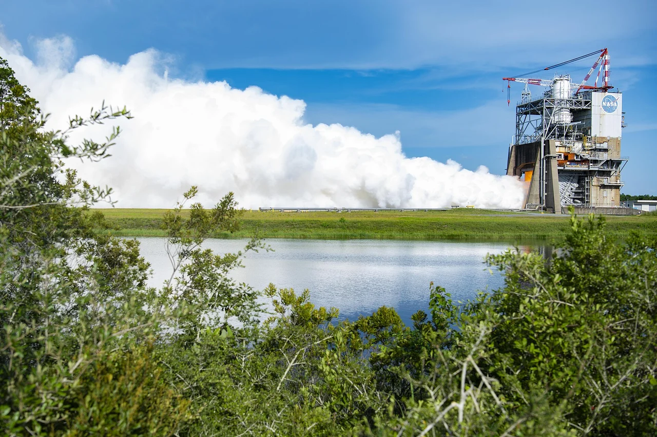 An RS-25 engine firing during a NASA ground test, with exhaust crossing the test stand