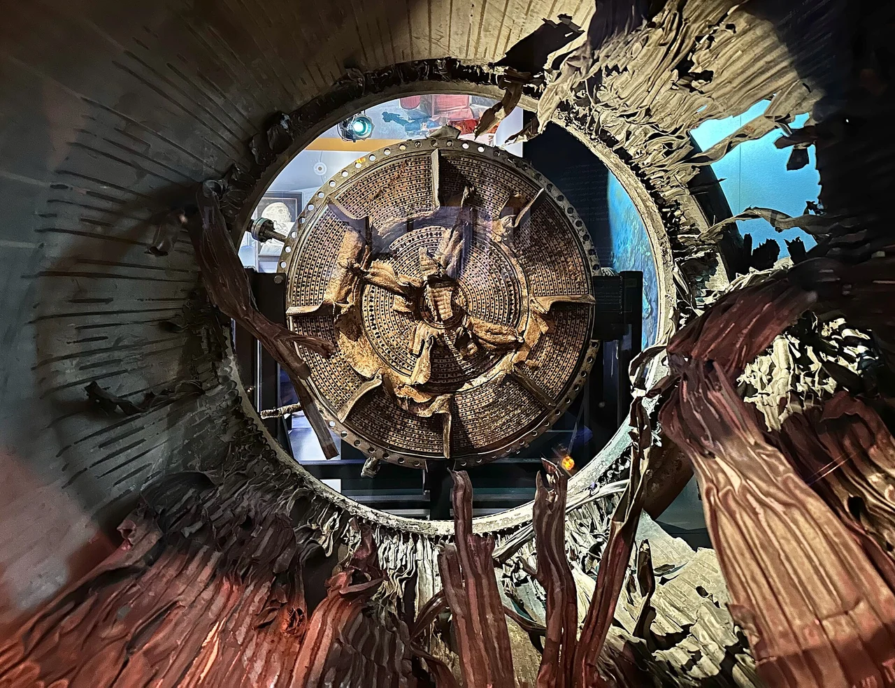 A recovered F-1 injector face with many visible injection openings, seen through damaged engine hardware