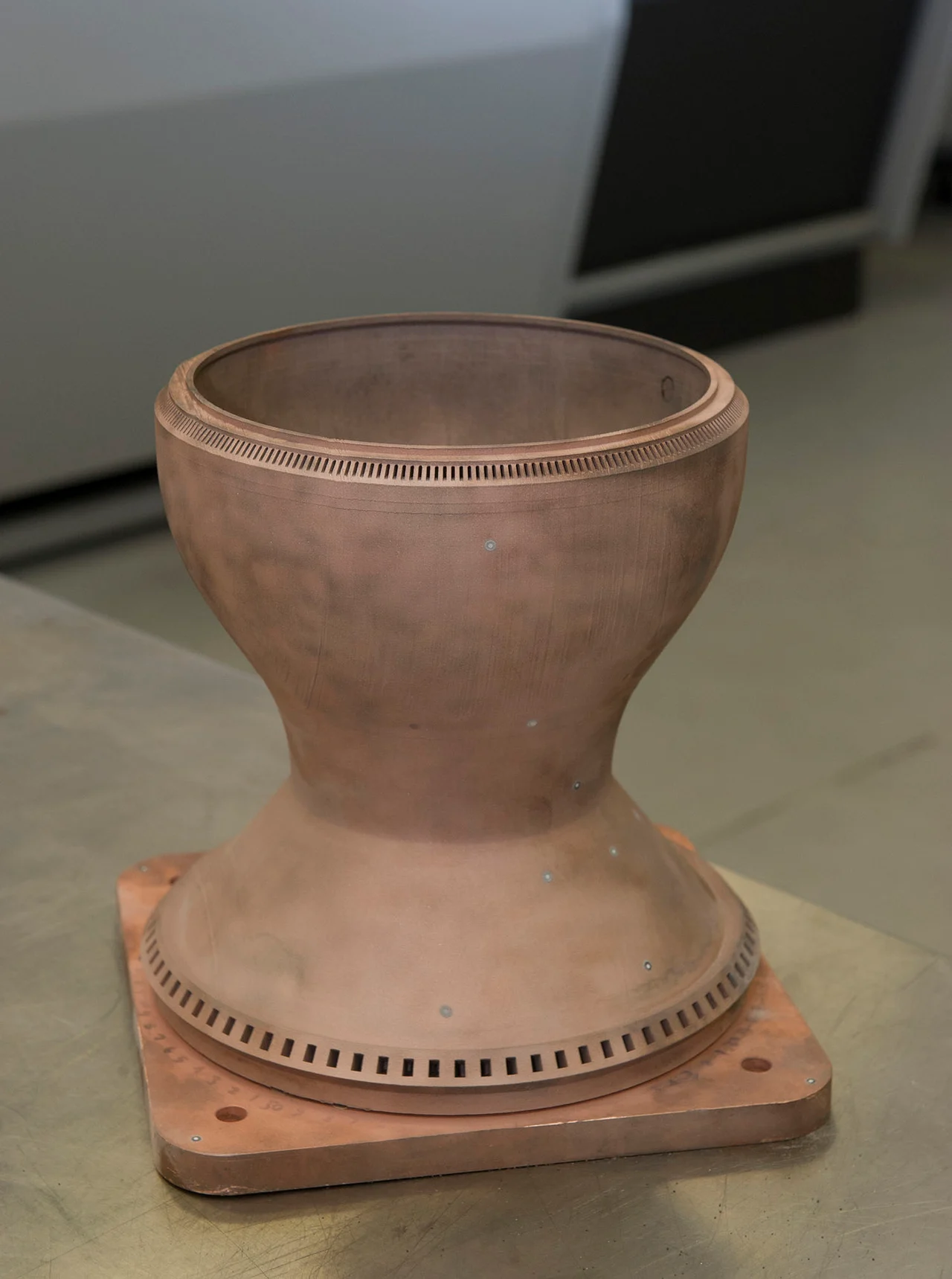 A copper-alloy rocket chamber liner with closely spaced coolant openings visible around its rims