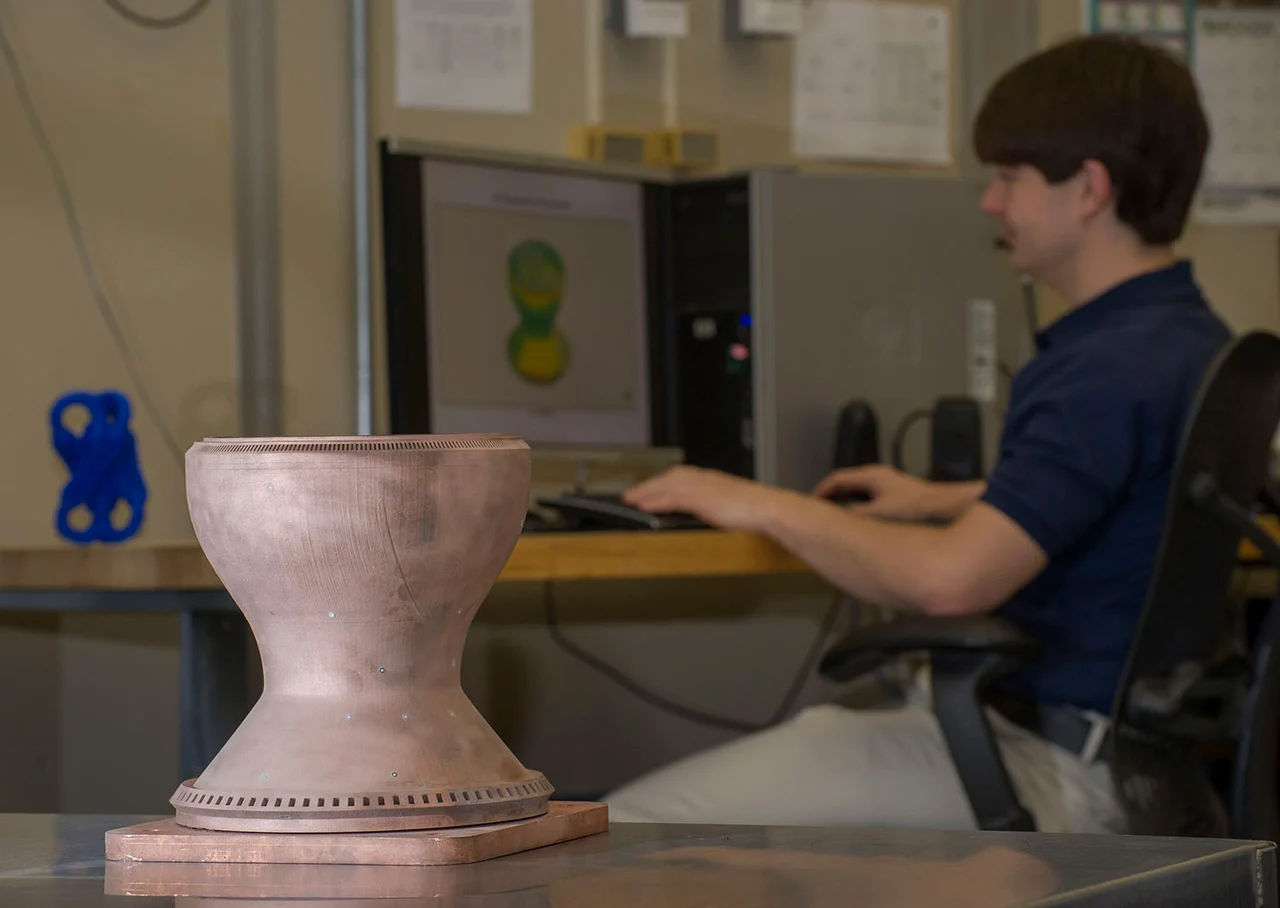 A NASA researcher beside a printed copper chamber liner and a computer showing its scanned shape