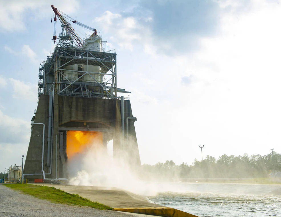 An RS-25 engine fires downward from the Fred Haise Test Stand, with exhaust and water vapor below